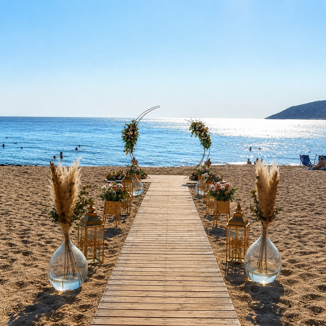 Boho στολισμός γάμου σε παραλία με ξύλινο διάδρομο, λουλούδια και φανάρια στο ηλιοβασίλεμα.